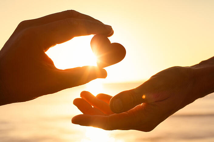 Eine Hand gibt einer anderen ein Herz im Sonnenlicht 