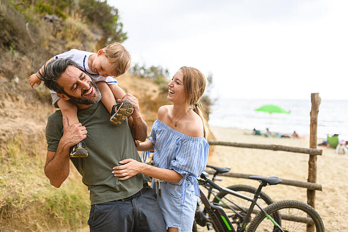 Familie mit Kleinkind und Rädern am Rande eines Strandes
